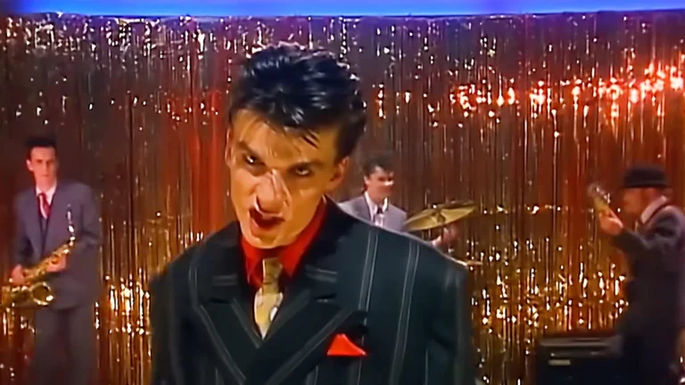 Dr. Robert of the Blow Monkeys performing on stage in a suit with the band behind him