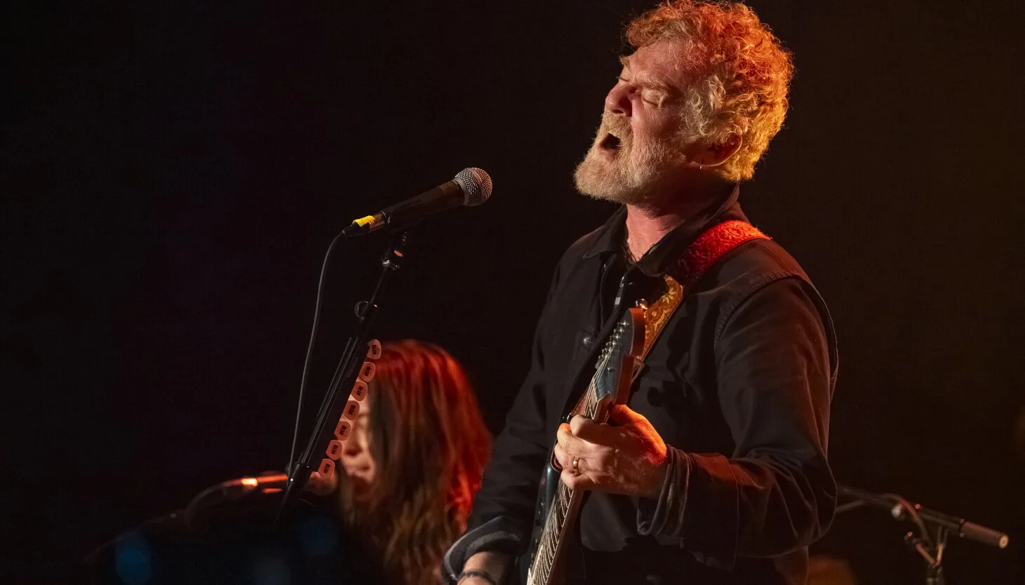 Glen Hansard performing on stage with a guitar during a concert