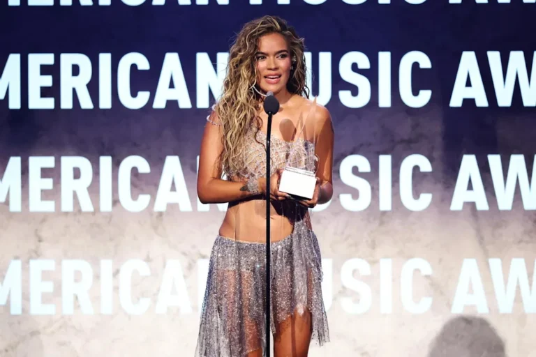 Karol G performs onstage at the American Music Awards in a silver outfit amid a snowy stage set