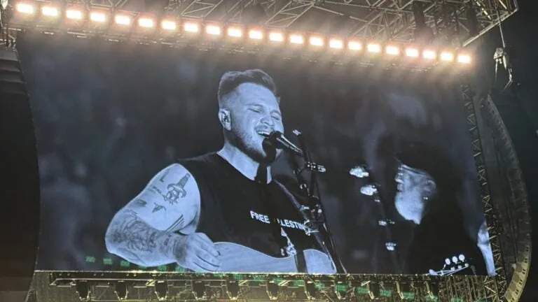 Zach Bryan performing at Gillette Stadium with a large band on a field stage