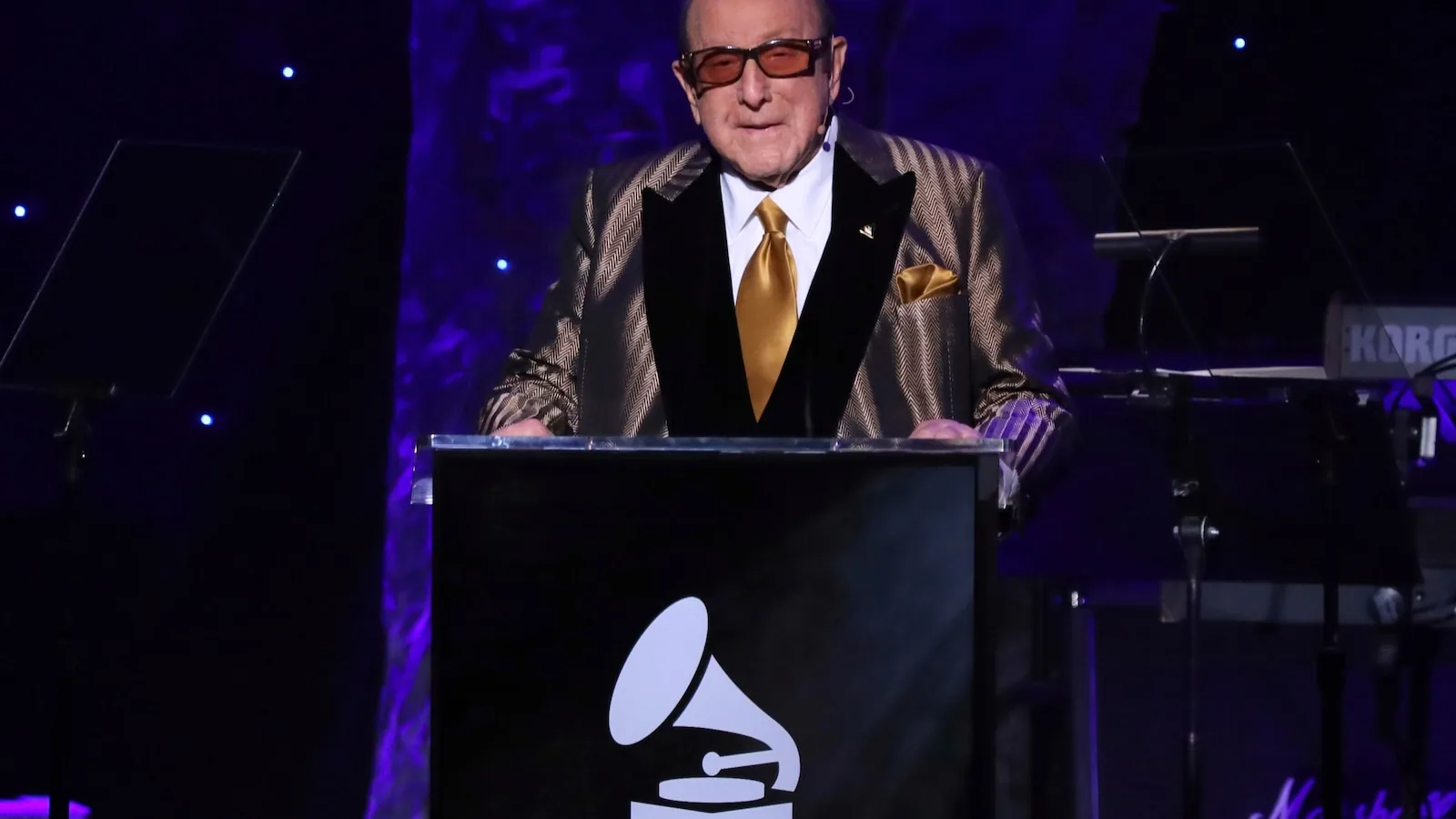 Clive Davis smiles at a music industry event with performers and guests in the background